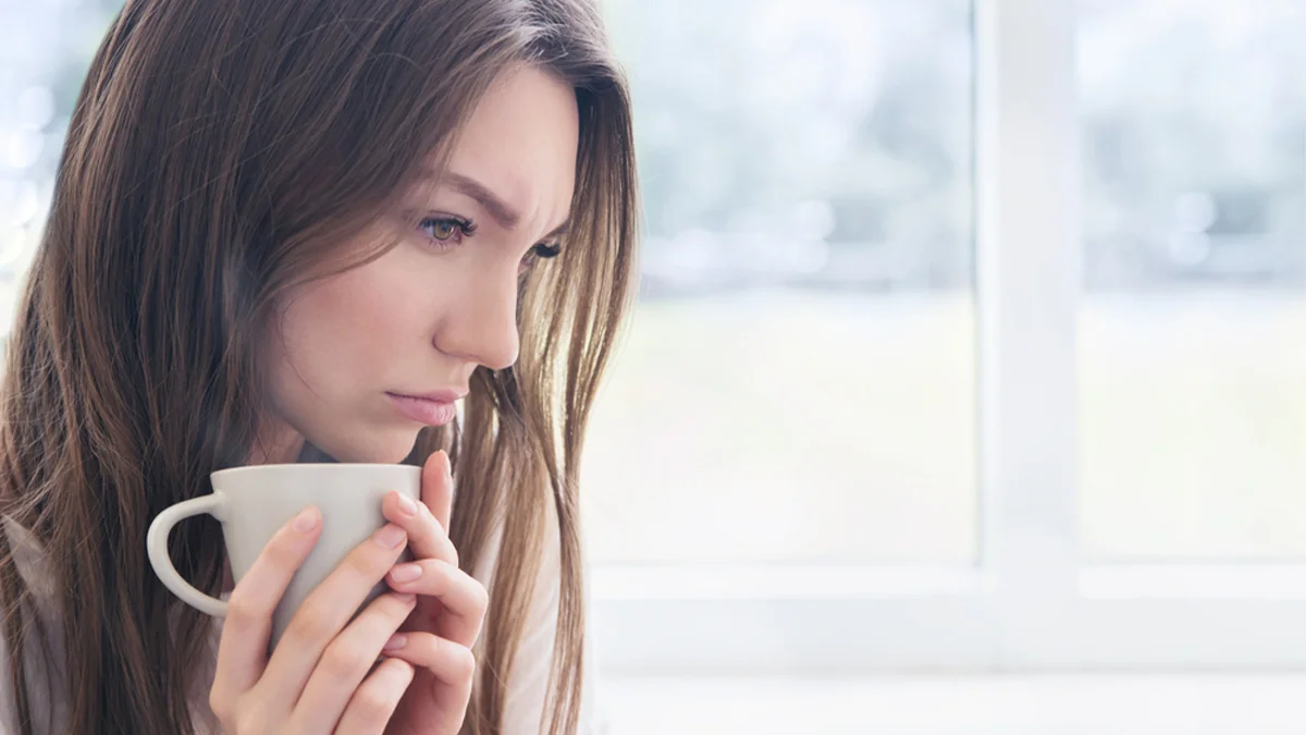 Woman staring off in the middle distance and holding a coffee mug. Mental health conditions can increase the risk of addiction.