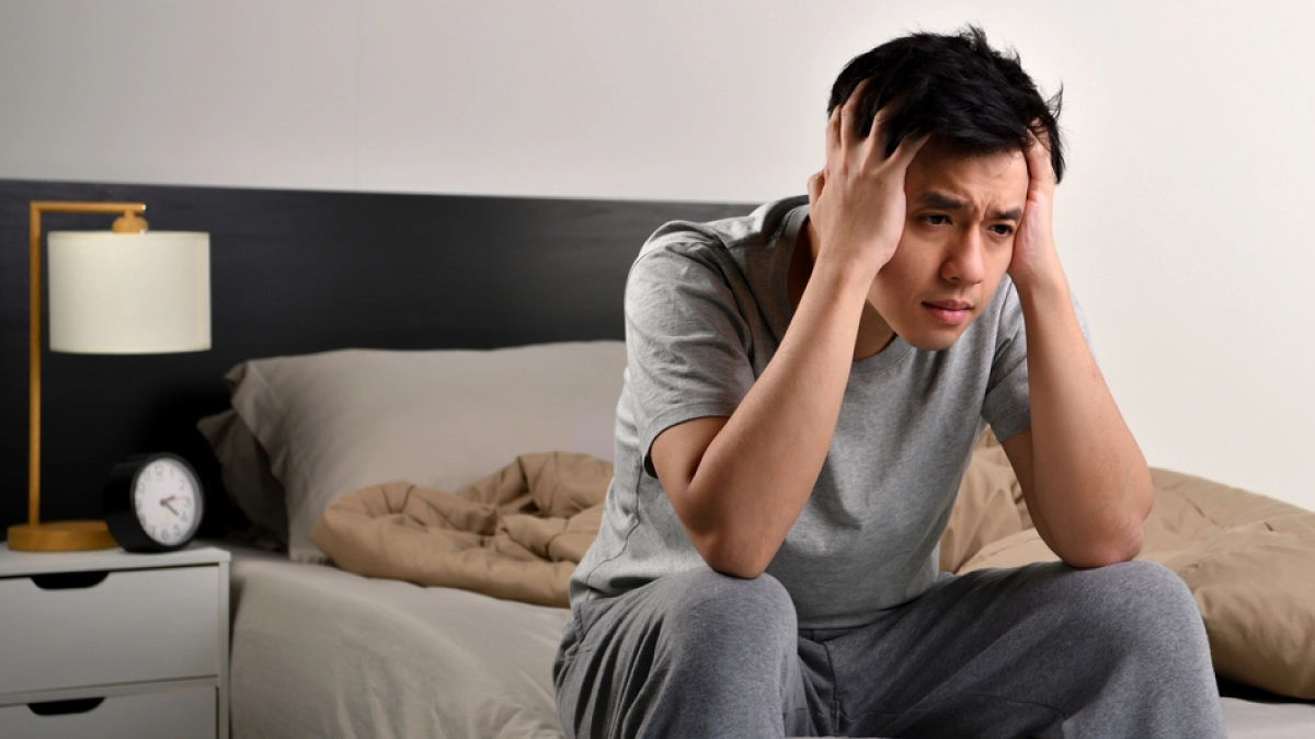 Man with anxiety sitting on bed with hands holding his head