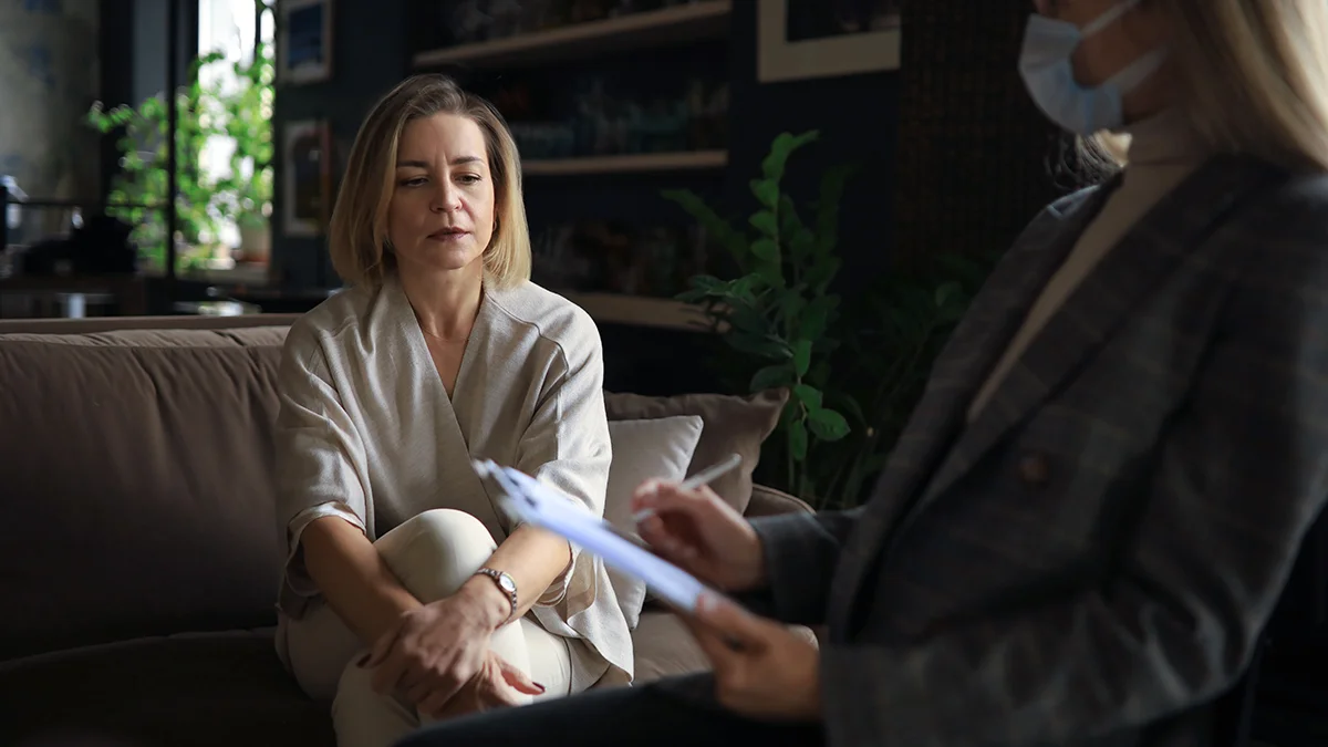 woman sits on a couch, looking contemplative during a therapy session.