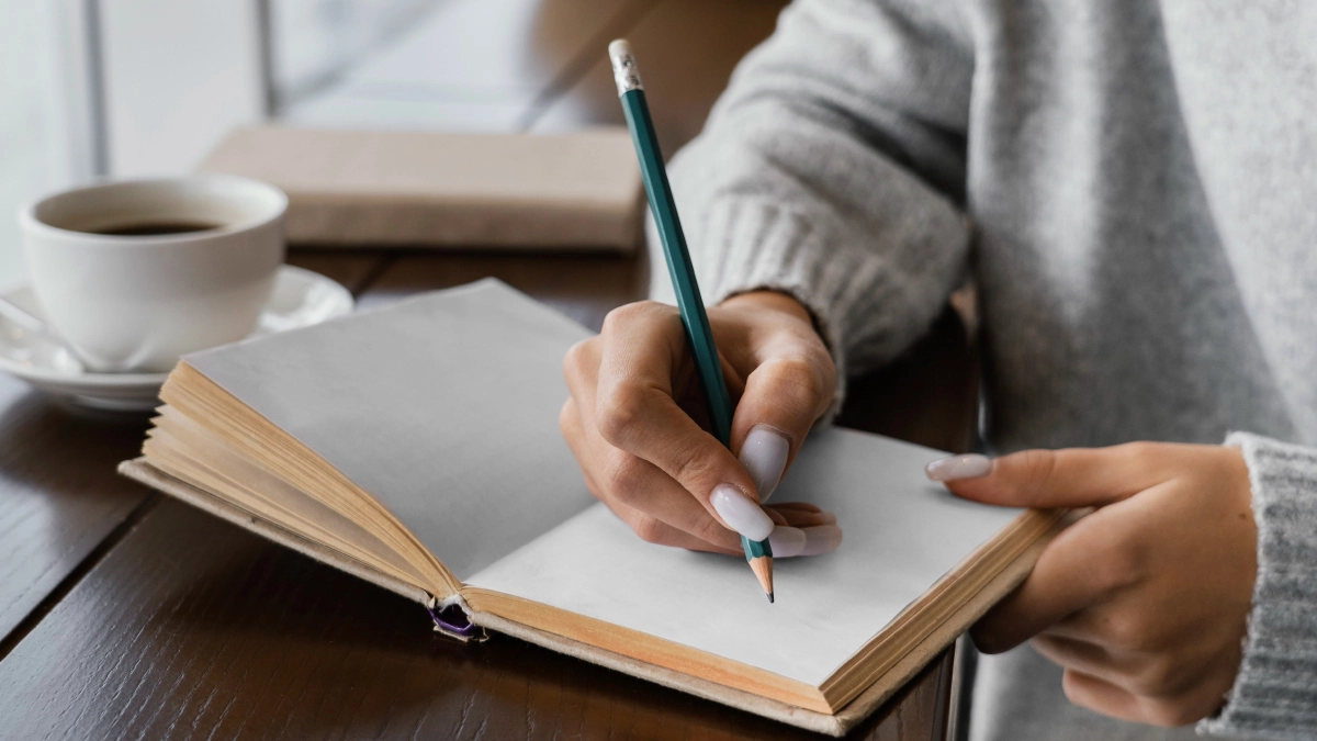 A close-up of a person writing in a journal with a pencil.