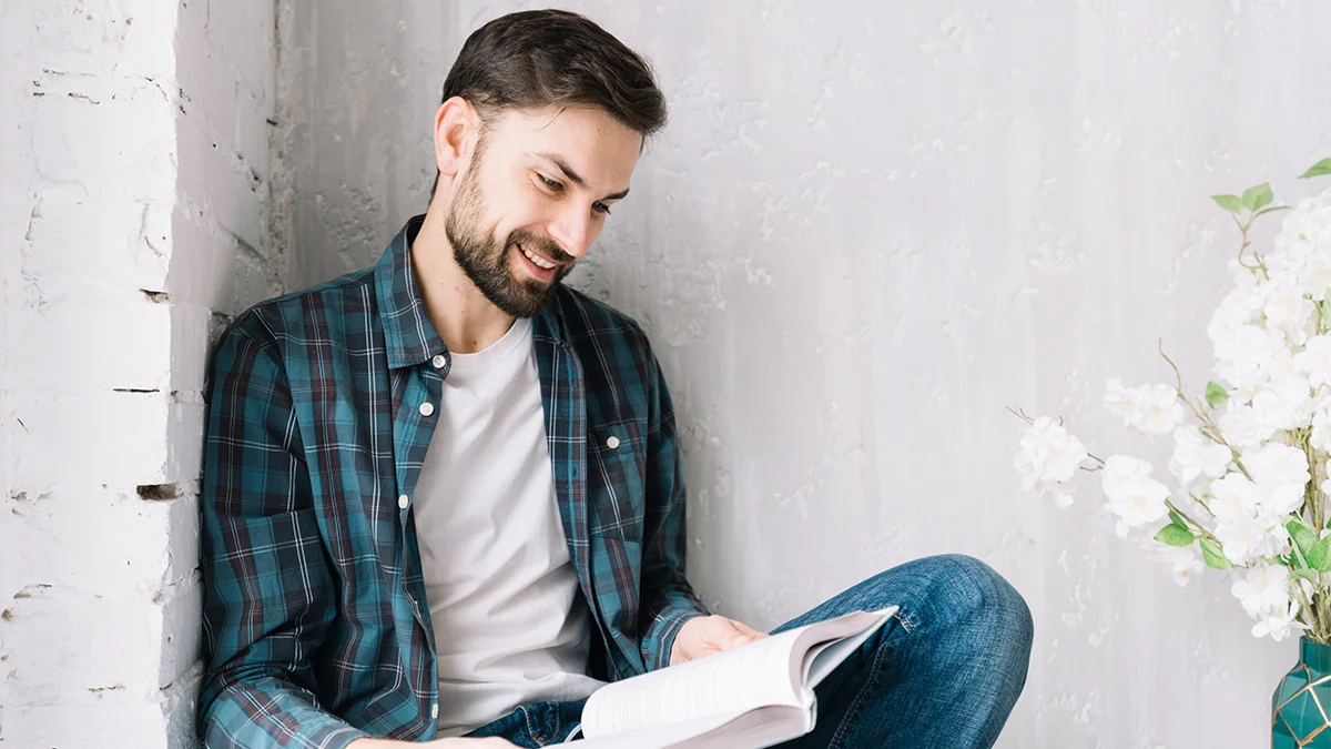 man reading a book with his back to the wall